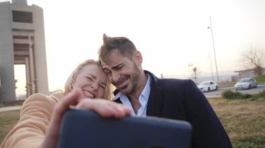 Funny middle aged couple taking selfie looking at cell phone. Smiling and laughing partner goofing around with face. Good memories of couple relationship. Video of wife and husband outdoors.