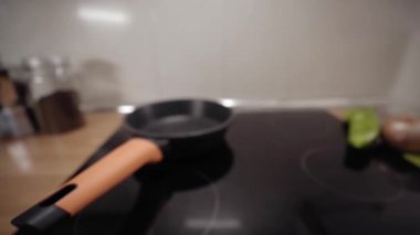Woman puts oil in the frying pan. Young woman cooking at home with a modern stove hood. Shot focused on the oil pan. People preparing healthy food in the kitchen of an apartment. Close up.