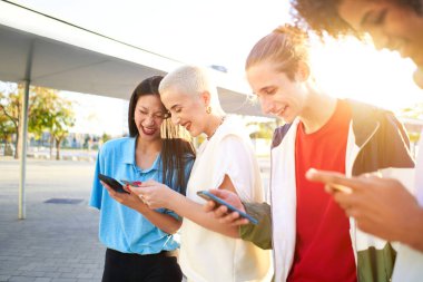 Group of young teenager friends chilling out together using smartphone social media concept. Focus is on shaved hair girl. High quality photo