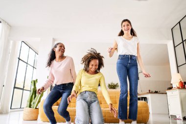 Üç komik bayan arkadaş evdeki kanepede dans edip şarkı söylüyor. Çok ırklı mutlu kadınlar oyun oynar ve hayatın neşesini kutlarlar. Neşeli kızlar evde birlikte eğlenirler. - Evet. Yüksek kalite fotoğraf