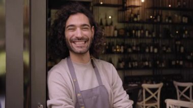 Close up video young adult local small business owner looking at camera. Happy male bartender with positive attitude. Cheerful worker smiles while standing leaning on bar door. Confident people. 