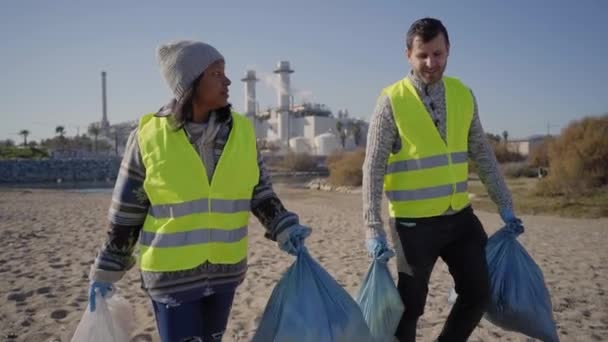 两名年轻的积极分子拿着垃圾袋聊天和走路 为地球工作的夫妇 清理志愿者在大自然中捡垃圾 环境保护的概念 — 图库视频影像
