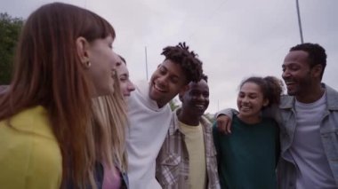 Young group of happy multiracial friends chatting with each other, hugging and laughing outside. Tourism, travel, leisure and teenage concept. People spending quality time together.