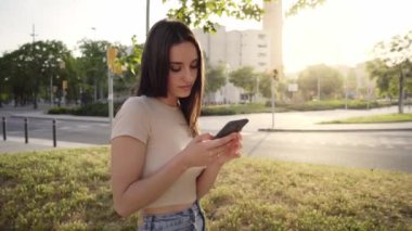 Serious woman chatting on cell phone with friends. Beautiful and focused people outdoors. Attractive young girl using mobile while waiting for date in city park. Empowered woman. Park city in Europe.