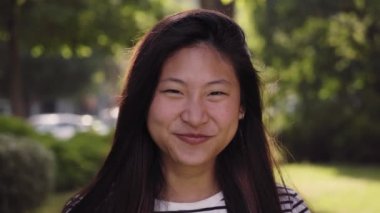 Close up of young Asian girl smiling looking at camera. Cute woman laughing standing on street city lifestyle. Beautiful happy female outdoors. Funny lady emotional expression on urban background. 