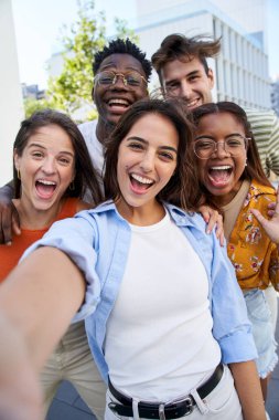 Vertical selfie young excited friends looking at camera happy. Smiling Group of people having fun together outdoors. Crazy community of college students. Modern lifestyle of multicultural people.