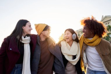 Çok ırklı mutlu arkadaşlar kucaklaşıp eğleniyorlar. Gülümseyen gençler birlikte gülüyor ve eğleniyorlar. Neşeli meslektaşlar, çok ırklı Erasmus öğrencileri kışın dışarıda toplandılar..