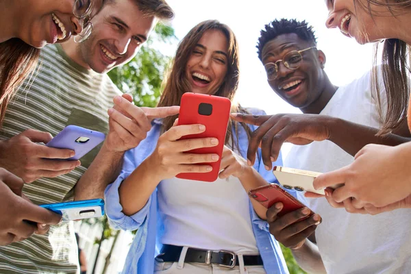 携帯電話で面白いリールを見ながら 多人種の若い学生を笑顔グループの低角度ビュー 人々を見て笑うと電話を指して集めました 社会関係と友情 — ストック写真