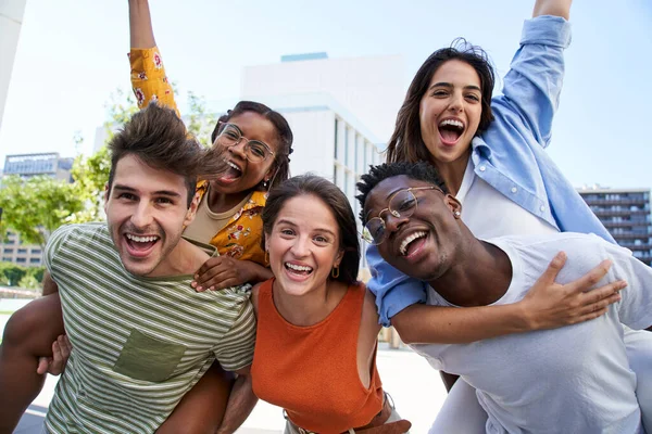 照片上快乐的年轻朋友看着相机兴奋极了 一群同学在外面玩得很开心 大学生的疯狂社区 多元文化的人拥抱和骑背 — 图库照片