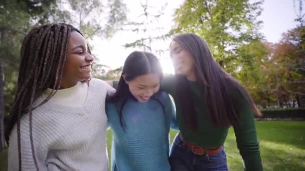 晴れた春の日に屋外で楽しんでいる3人の女の子のビデオ 中国系アジア系黒人アフリカ系アメリカ人と白人系アメリカ人の女の子が集まって抱き合っていた 友人と自由な時間を楽しむ人々 — ストック動画