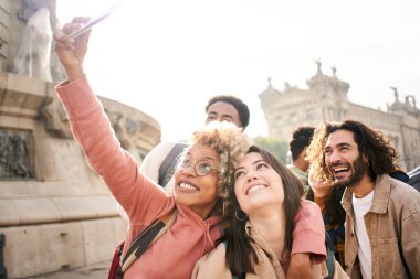 Genç çok ırklı arkadaşlar akıllı telefonlarıyla selfie çekiyorlar ve açık havada eğleniyorlar. Yüksek kalite fotoğraf