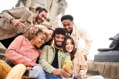 Adam çok ırklı arkadaşlarına akıllı telefondan bir video gösteriyor. Bir grup insan mobil veya akıllı bir cihazdan bir şey izliyor. Yüksek kalite fotoğraf