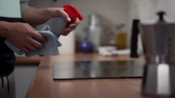 用男性手用微纤维布喷涂和清洁玻璃陶瓷的密闭 公寓里的家务活厨房地板上的人清洁感应吸盘 做家务活的人 — 图库视频影像