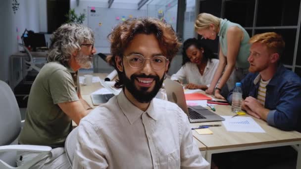 快乐的年轻领导人坐在那里 看着办公室里的摄像机 在工作会议上带着眼镜和胡子的生意人微笑 努力工作和有进取心的男性形象 工作场所快乐的人 — 图库视频影像