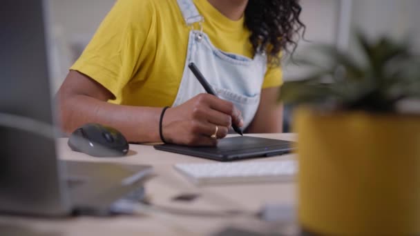 アフリカ系アメリカ人の女性がコンピュータ用のタブレットを使って作業している フォーカスは背景で撮影しました 自宅で机の上で練習している自営業の女の子 カジュアルな若者は屋内で生活を得る — ストック動画