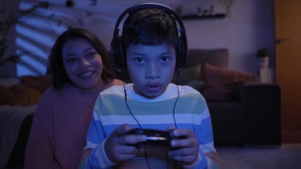 幸せなラテン語の母親と息子は夜のリビングルームでビデオゲームをプレイ 小さな男の子と若い母親が家でオンラインゲームに勝つために興奮しています 子供時代 家庭の甘い家の概念 — ストック動画