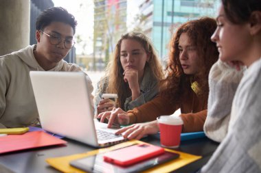 Ciddi çeşitli arkadaşlar dizüstü bilgisayarla birlikte çalışırlar. Sınıf arkadaşları kampüsün dışında kahve içerek sınav hazırlıyor. Kafeterya terasında bilgisayar kullanan odaklanmış çok ırklı genç insanlar.