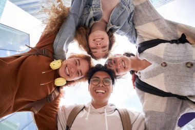 Erasmus Uluslararası Üniversite öğrencileri kameraya bakıp birbirlerine sarıldılar. Bir grup gülümseyen genç insan aşağı bakıyor. Düşük açı. Boşluğu kopyala.