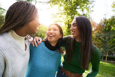 Güneşli bir bahar gününde dışarıda eğlenen üç kızın portresi. Çinli siyahi Afrikalı Amerikalı ve beyaz kızlar bir araya gelip kucaklaştılar. İnsanlar arkadaşlarıyla boş zamanlarının tadını çıkarıyorlar..