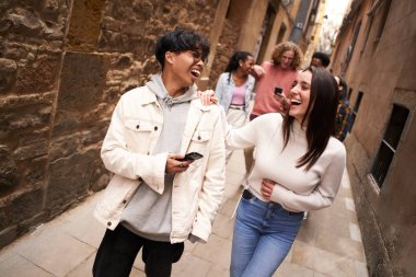 Group of happy friends using phone outdoors while walking al laughing. High quality photo