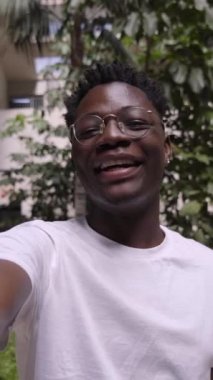 Dikey POV genç Afrikalı Amerikalı gülümseyen ve kamera karşısında konuşan neşeli genç bir adam. Telefona bakan mutlu insanlar. Siyah adam kendini cep telefonuyla kaydediyor ve bir şeyi işaret ediyor. 