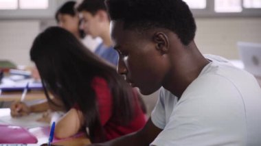 Sınıfta sınava giren genç Afrikalı Amerikalı öğrenci. Dil sınıfındaki siyah çocuk. Sınıf arkadaşları arka planda bir masada oturuyor. Eğitim kavramı ve gelecek nesiller.