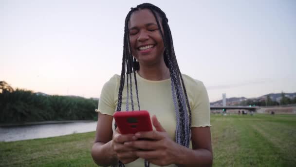 Jovem Mulher Africana Alegre Usando Smartphone Enquanto Está Sentado Livre — Vídeo de Stock