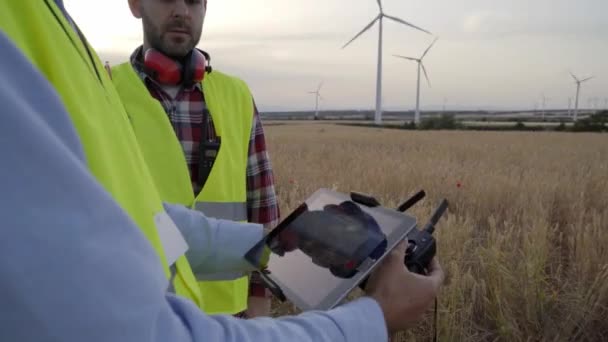 遠隔操作とクアッドコプターを保持するオペレーターの手 作業中のタブレットドローンを使う男性技術者 再生可能エネルギー風車分野のデータドロンを制御する技術者 — ストック動画