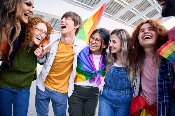 Group of excited young friends enjoying together on gay pride day. Joyful people gathered from LGBT community hugging laughing outdoors. Generation z and open minded.