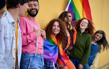 Duvarda sarı duran gülen genç arkadaşların portresi. LGBT topluluğu mutlu insanlar eşcinseller gününü gökkuşağı bayraklarıyla kutluyor. Nesiller boyu eğlence partisi homoseksüelleri.