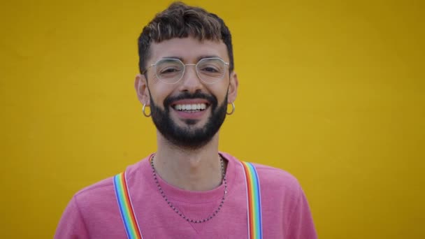 虹のLbtのサスペンダーを持つ陽気な若い白人男性の笑顔を閉じます ビデオ黄色の背景のためにポーズゲイの人々 陽気なゲイのひげを生やした人幸せなスタジオは孤立した 千年世代 — ストック動画