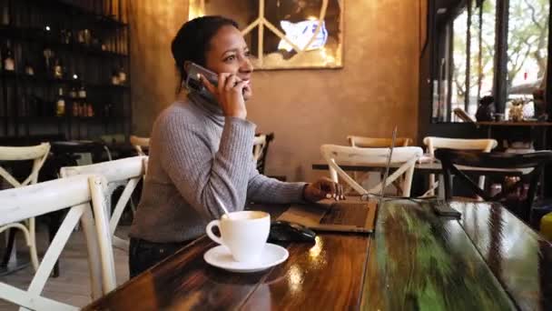 Genç Siyah Kız Kahve Dükkanının Içinde Dizüstü Bilgisayarın Önünde Telefonla — Stok video