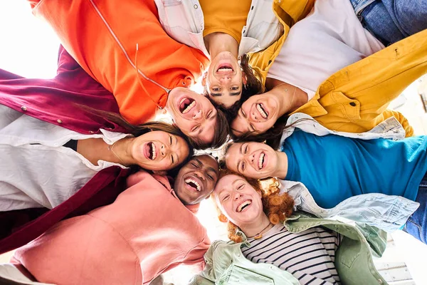 Large multiracial group of smiling young people standing hugging looking at camera. Group of cheerful people in circle looking down. Low angle view. Copy space.