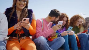 LGBT topluluğundan bir grup genç arkadaş cep telefonu kullanıyor ve eşcinsel onur festivali gününü birlikte kutluyorlar. Mutlu insanlar sosyal ağları kontrol etmek için dışarıda toplandılar. Z nesli ve uygulamalar.