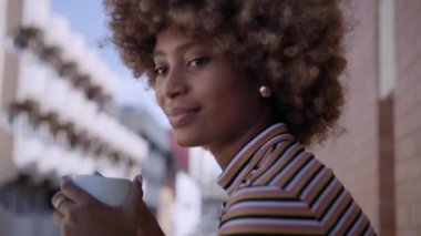 Afro saçlı mutlu siyah kadın gülümseyen kameraya bakıyor. Neşeli Afrikalı Amerikalı kız elinde bir fincan kahve tutuyor. Olumlu ifadeli bir kadın portresi. Boşluğu kopyala.