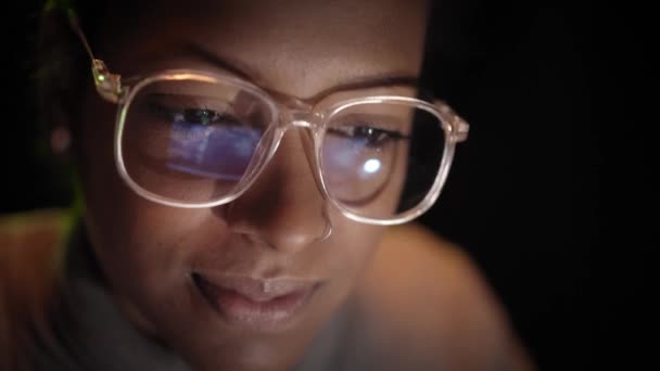暗闇の中でノートパソコンで働いているアフリカ系アメリカ人のハッカー女性の眼鏡にコンピュータ画面の反射の終わり 若者とコンピュータネットワークとインターネットのセキュリティ — ストック動画