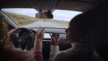 Farklı kadınlar ikincil yolda araba sürerken mutlu bir şekilde şarkı söylüyorlar. Canlı müzik arabasıyla dans eden iki genç kız kırsaldan geçiyor. İnsanlar eğlenmekten zevk alır. Dikiz aynası. Yavaş çekim.