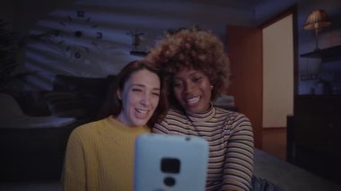 Mutlu, eşcinsel, evli, kadın, gülümseyen ve cep telefonunu video görüşmesi için evdeki oturma odasında kullanan bir çift. Birlikte hayatın tadını çıkaran çok ırklı lezbiyen çift ilişkisi. LGBT içerideki insanlar. 
