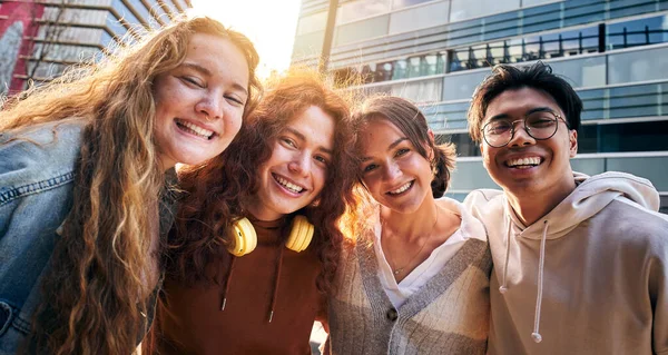 Erasmus Uluslararası Üniversite öğrencileri kameraya bakıp açık havada birbirlerini kucaklıyorlar. Fotoğraf için poz veren dört gülümseyen genç arkadaş grubu. Avrupa 'da gezen neşeli insanlar.