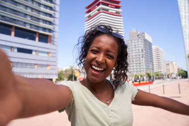 Genç Latin bir kadın gülen selfie 'yi şehir ortamında dışarı çıkarıyor. Kameraya çekilen mutlu Afro-Amerikan kız resmi. Neşeli insan eğleniyor. Yaz anıları. Pozitif duygu kavramı