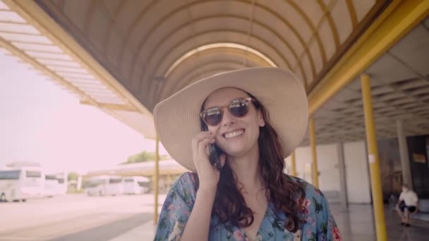 穿着夏装的快乐的年轻女子在车站散步 用手机聊天 微笑的女孩在外面一边等公共交通工具 一边用手机聊天 度假愉快的人 — 图库视频影像