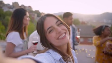 Çatıdaki partide arkadaşlarıyla sosyal medya için video çeken gülümseyen Avrupalı genç kızın POV selfie 'si. Dans eden ve şarap içen gruplar. Gençlerin ilişkileri