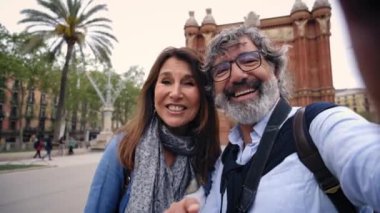 Olgun emekli çift, Avrupa turizm şehrinin parkında bekleyen akrabalarına telefonla video görüşmesi yapıyor. Sosyal ağlardaki arkadaşlar için tatil videosunda neşeli yetişkin evliliği..