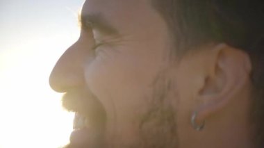 Kameraya gülümseyen yakışıklı beyaz adamın yakın portresi. Genç adam dışarıda, pozitif ve rahat bir tavırla anın tadını çıkarıyor. Neşeli milenyum insanları güneşli bir günde.