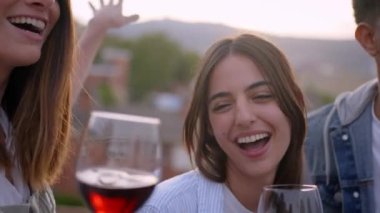 Gün batımında çatıda dans eden ve şarkı söyleyen farklı arkadaş gruplarını kapatın. Mutlu ve heyecanlı gençler ellerinde kırmızı şarapla yaz tatilinde dışarıda eğleniyorlar.. 