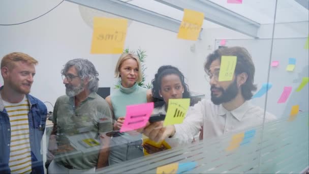 一群严肃的人聚集在办公室的一个岗位上讨论策略 头脑风暴式地做笔记 这是个多种族的团队合作计划 为初创企业规划一个业务 重点工作人员一起工作 — 图库视频影像