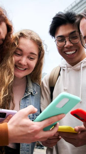 多人種の同級生のグループは 自分のスマートフォンを見てソーシャルメディアを共有しています 昼間は大学外での歓談 友達世代Zは携帯電話を使って楽しんでいます — ストック写真