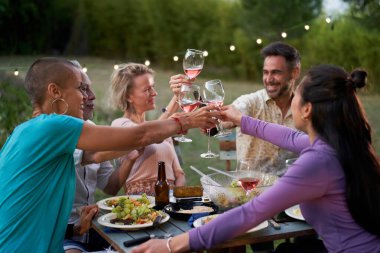 Mutlu arkadaşlar özel akşam yemeği partisinde arka bahçede kırmızı şarap içerek eğleniyorlar. Orta yaşlı insanlar lokantada birlikte bbq yemeği yiyorlar. Yemek yaşam tarzı konsepti. Gözlüklere odaklan. Yüksek kalite