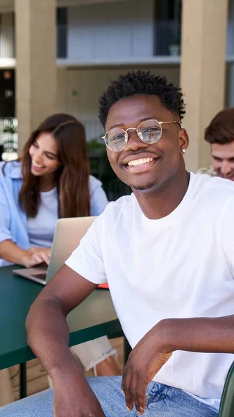 非常に幸せな黒い男の垂直方向の肖像画 笑顔とカメラを見て アフリカ系アメリカ人の学生は 同級生と大学のカフェテリアに座って笑っていました 大学のキャンパス内の人々 — ストック写真