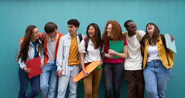 Bir grup gülümseyen, etnik çeşitlilikte üniversite öğrencisi derslere ara veriyor. Mavi duvara yaslanmış birbirlerine gülerek sarılan genç arkadaşlar. Nesiller z ve gençlik ilişkileri.